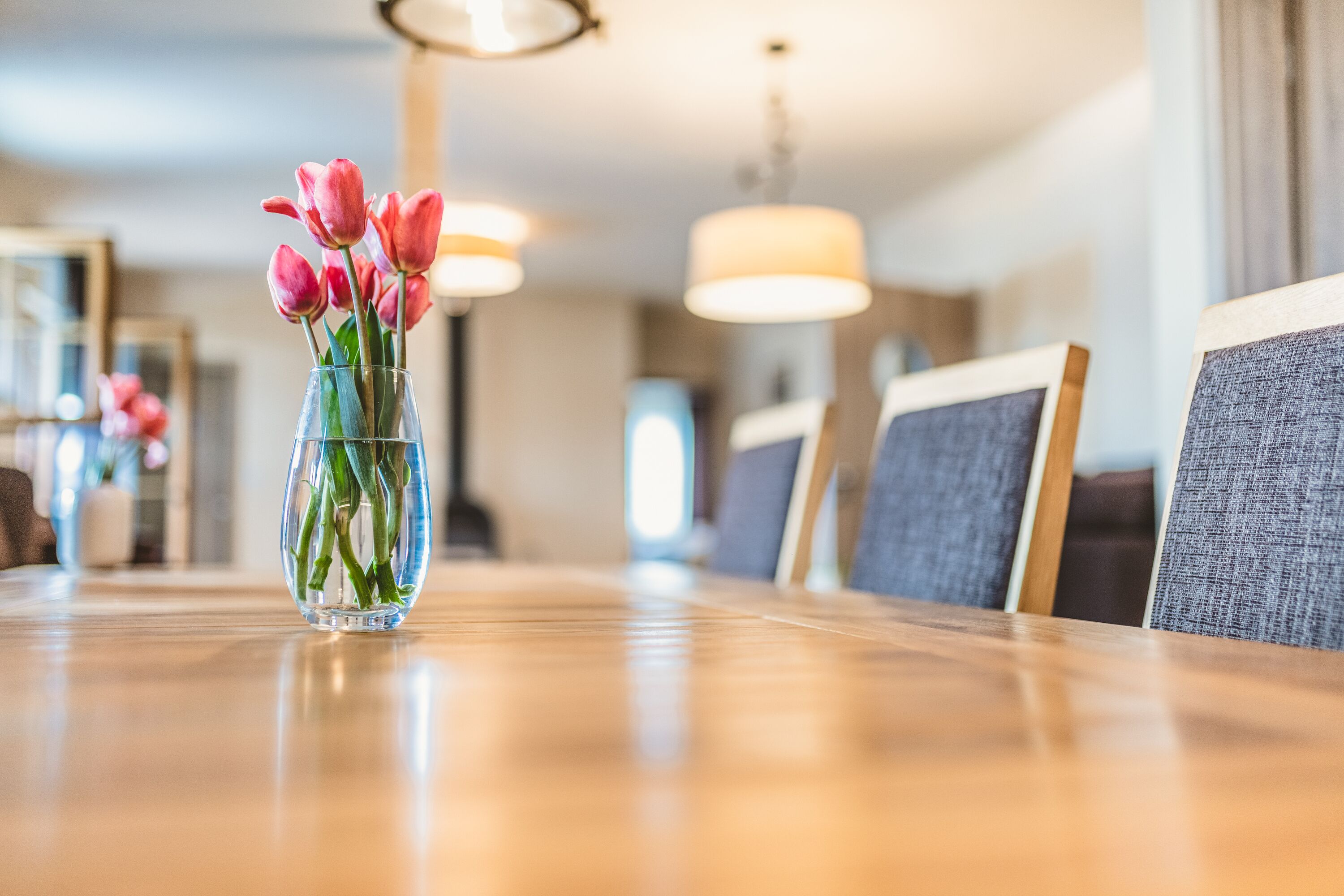Una mesa de comedor con un florero de vidrio transparente que contiene tulipanes rosados.
