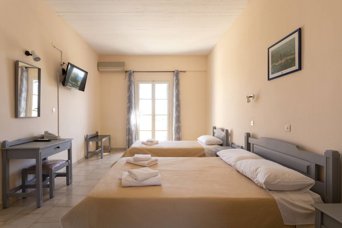 A hotel room with two beds, a desk, a chair, a television, and a window with curtains.