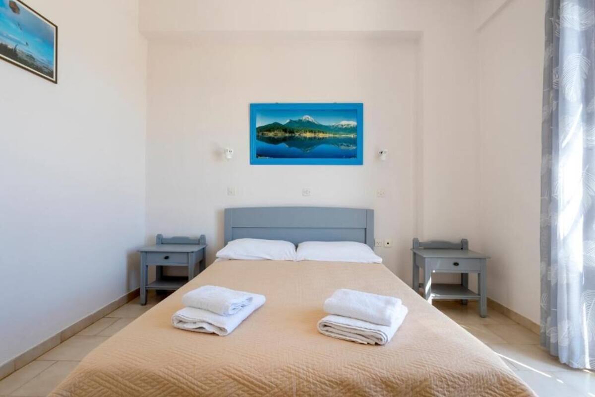 A bedroom with a bed, two nightstands, a painting on the wall, and a window with curtains.
