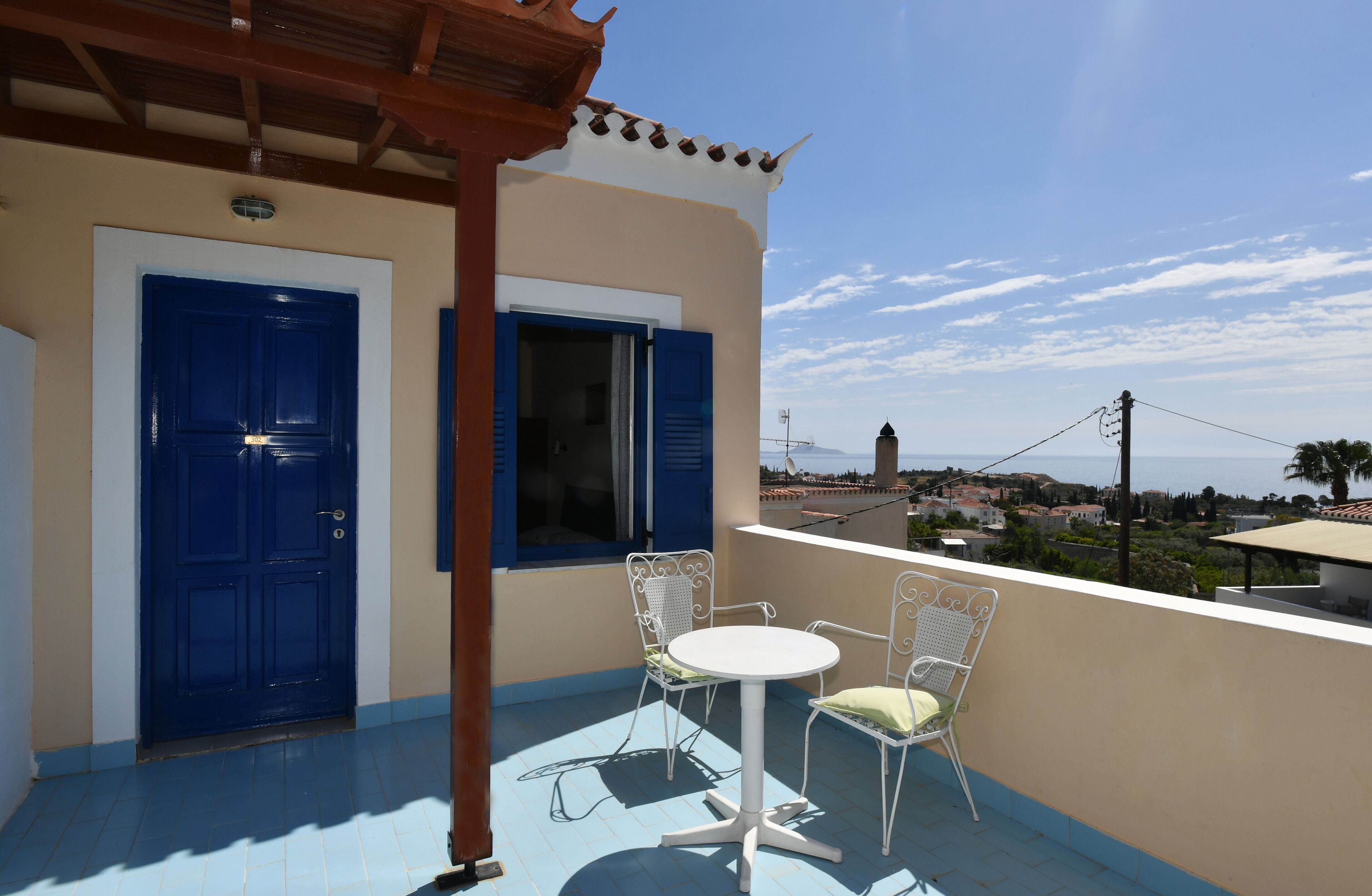 A balcony with a blue door, a window with blue shutters, and two white metal chairs.