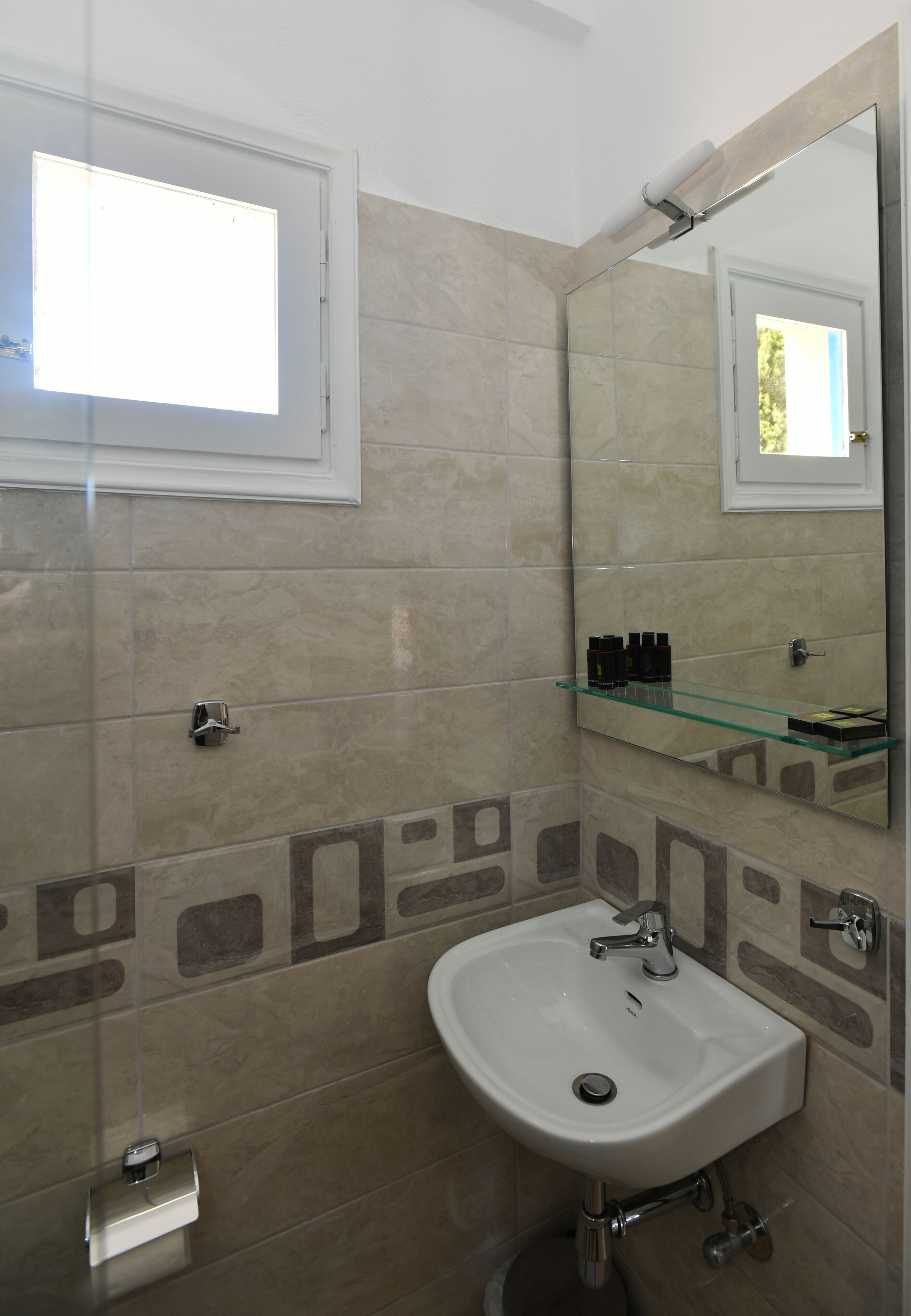 A bathroom with a glass shelf, a sink, and a mirror.