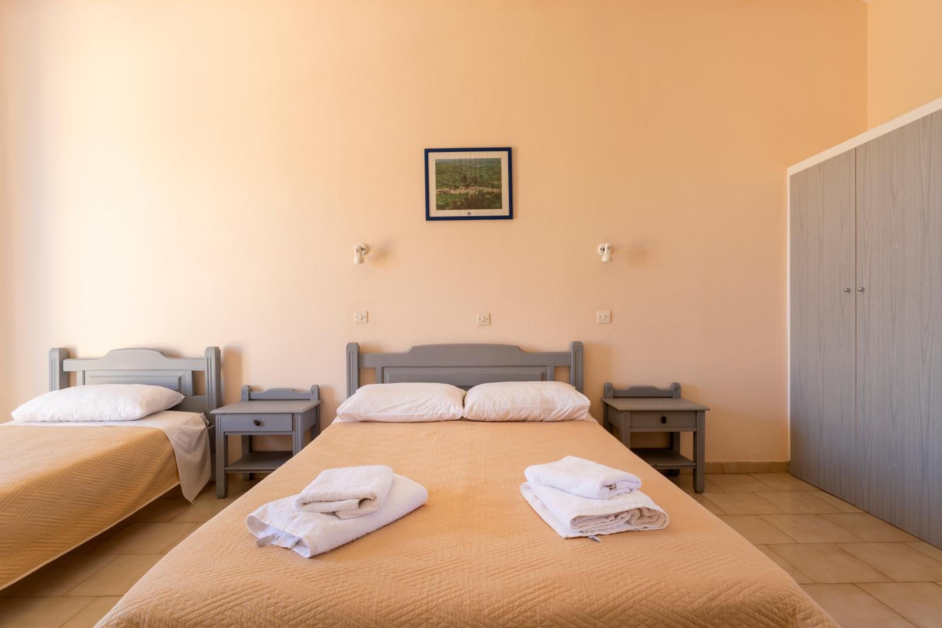 A hotel room with two beds, a wardrobe, and a framed picture on the wall.