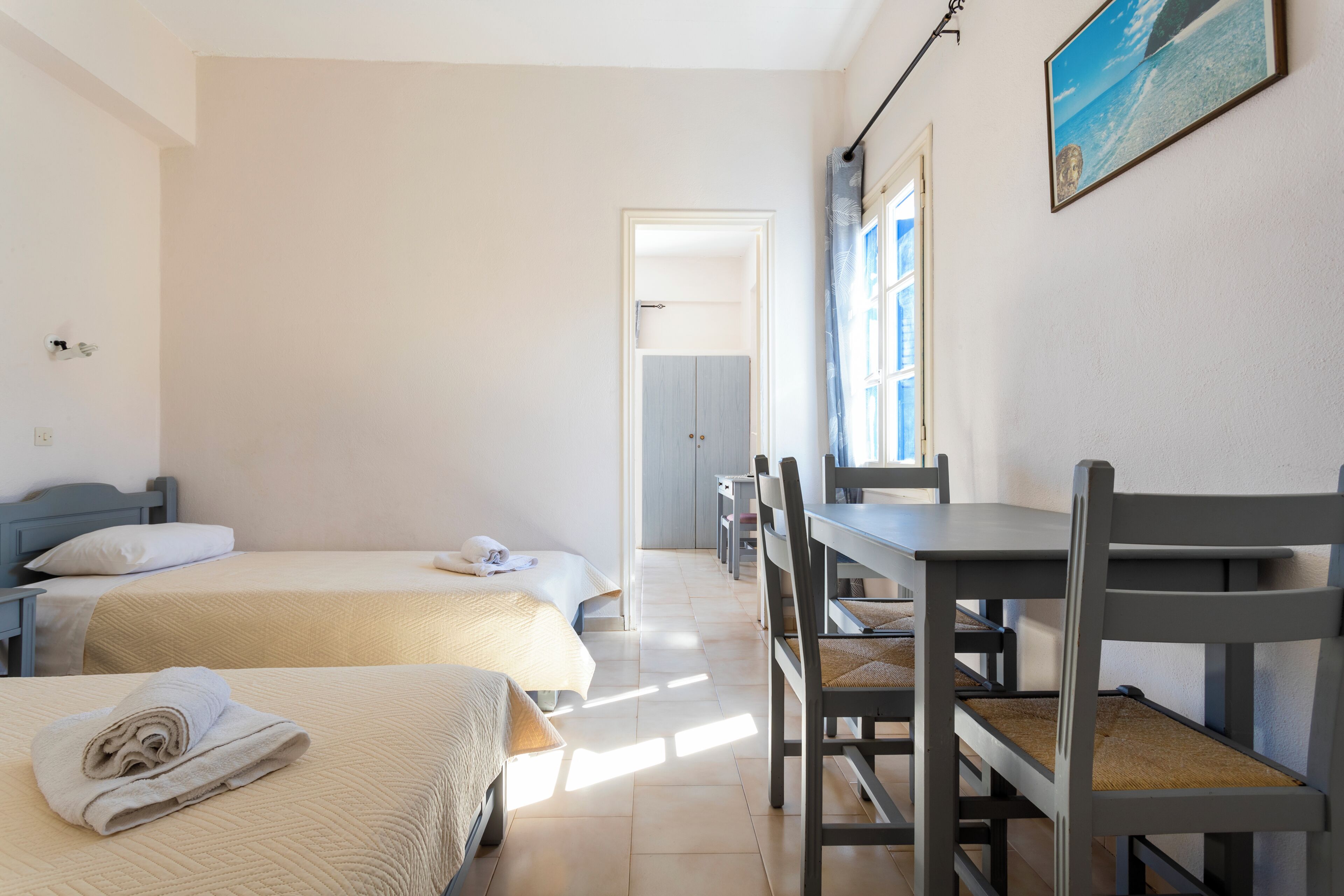 Une chambre d’hôtel avec deux lits, un bureau et une chaise. Il y a une fenêtre avec des rideaux et un tableau au mur.