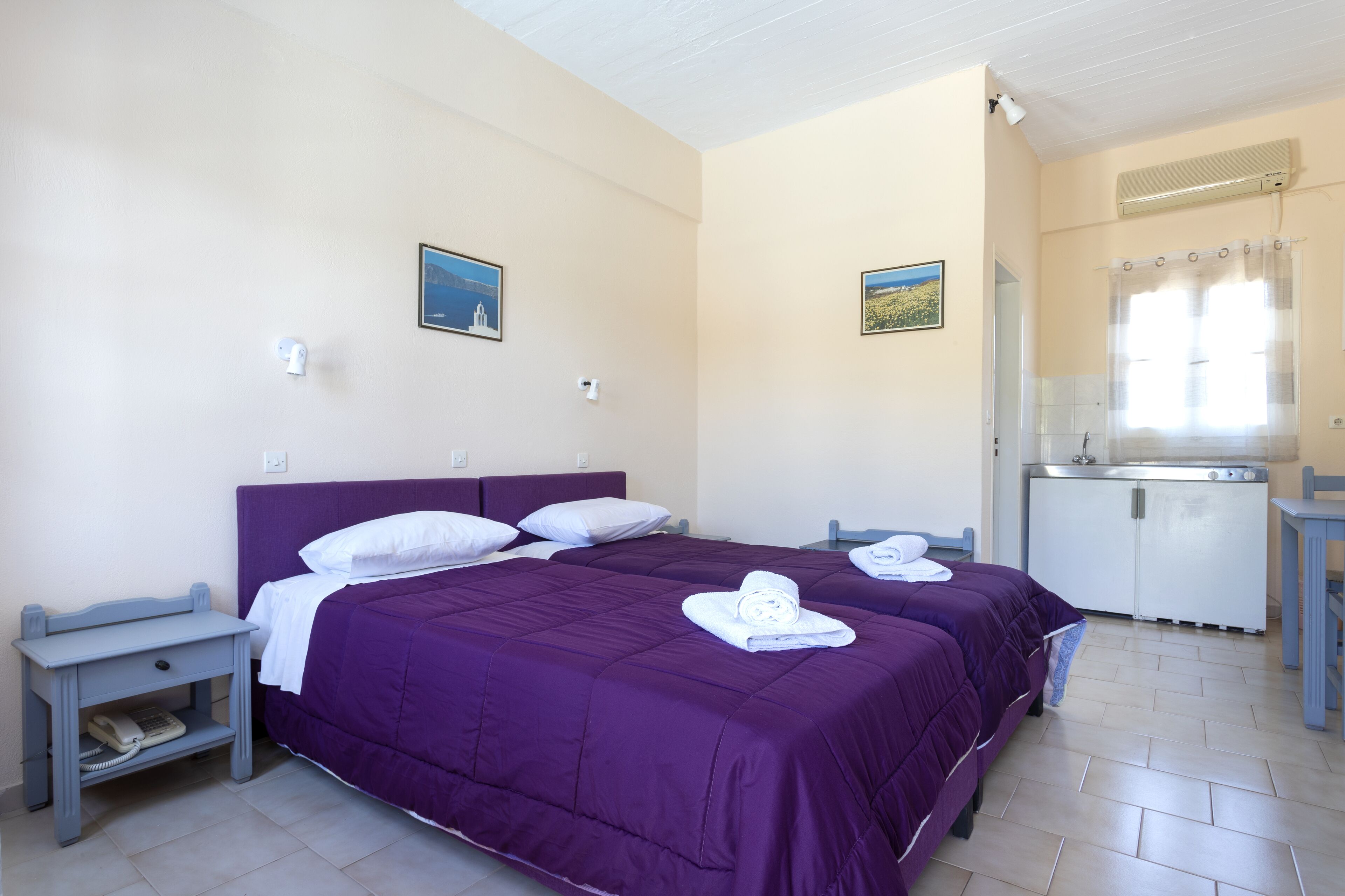 A bedroom with two beds, a small desk, and a kitchenette.