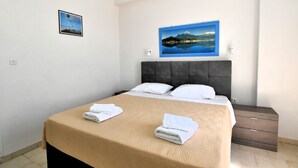 Un dormitorio con cama, dos almohadas, una mesita de noche y un cuadro colgado en la pared.
