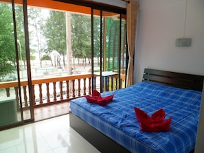 Habitación de hotel con un ventanal grande, cama con ropa de cama azul y balcón con vista a la calle y árboles.