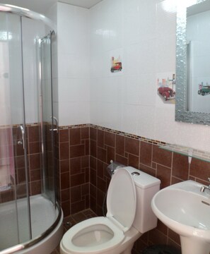 Un baño con cabina de ducha de vidrio, inodoro y lavamanos.