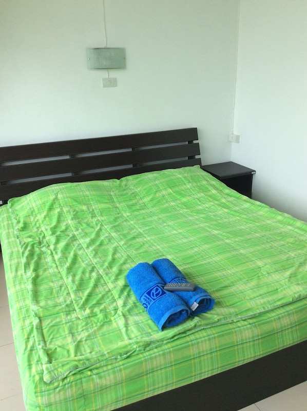 Una cama con una colcha verde a cuadros y dos toallas azules.