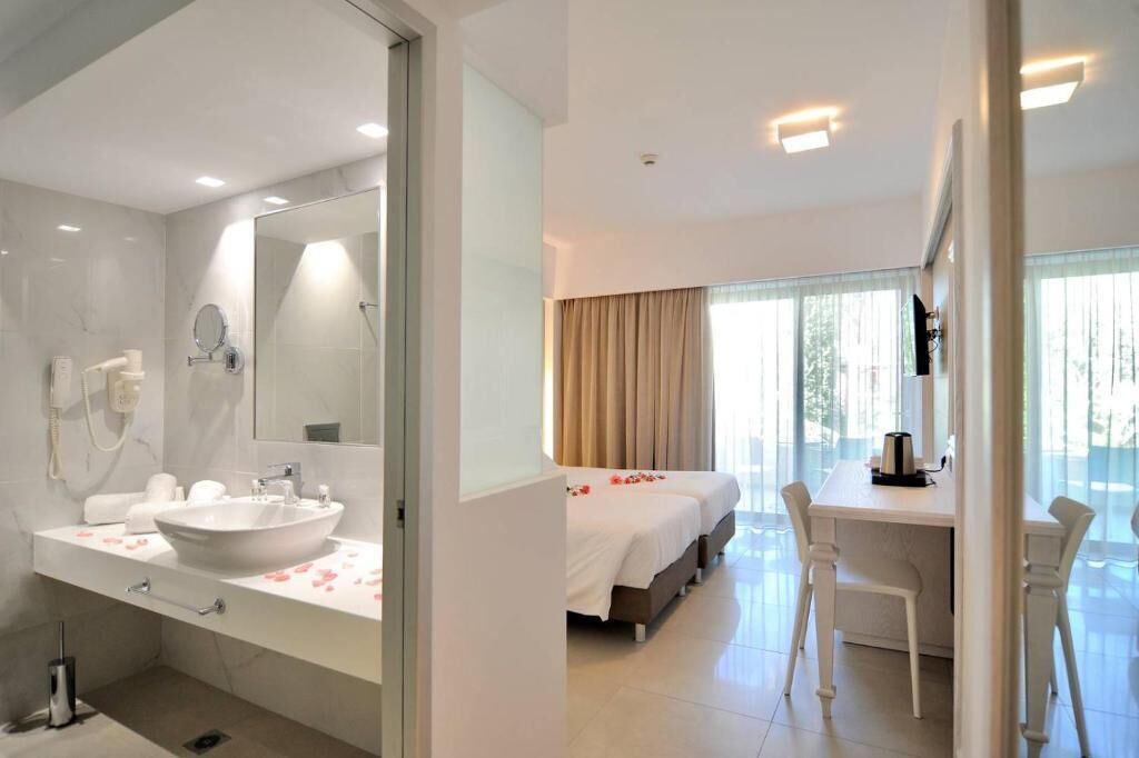 Una habitación de hotel moderna con un baño amplio, una cama con pétalos de rosa, un escritorio y un ventanal grande.