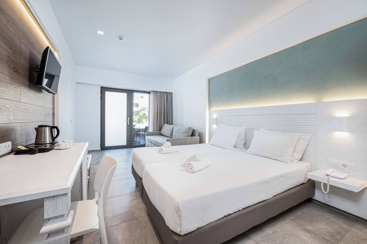 Una habitación de hotel moderna con una cama grande, un escritorio con televisor de pantalla plana, una cafetera y un teléfono en una mesita de noche.