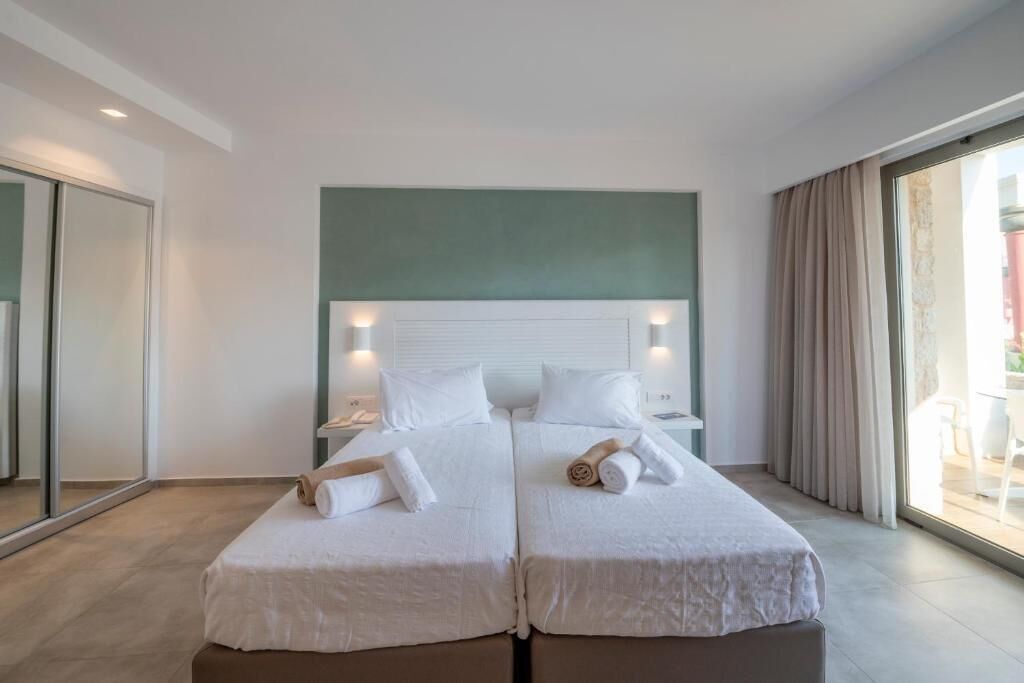 Una cama doble con ropa de cama blanca, un cabecero con iluminación integrada, una mesita de noche y vistas a un espacio exterior a través de una puerta de cristal.