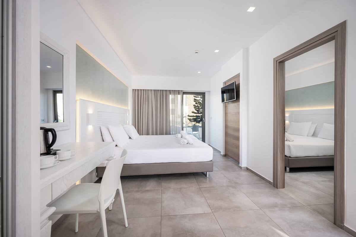 Una habitación de hotel moderna con una cama grande, un escritorio con una silla, un televisor de pantalla plana y un espejo amplio.