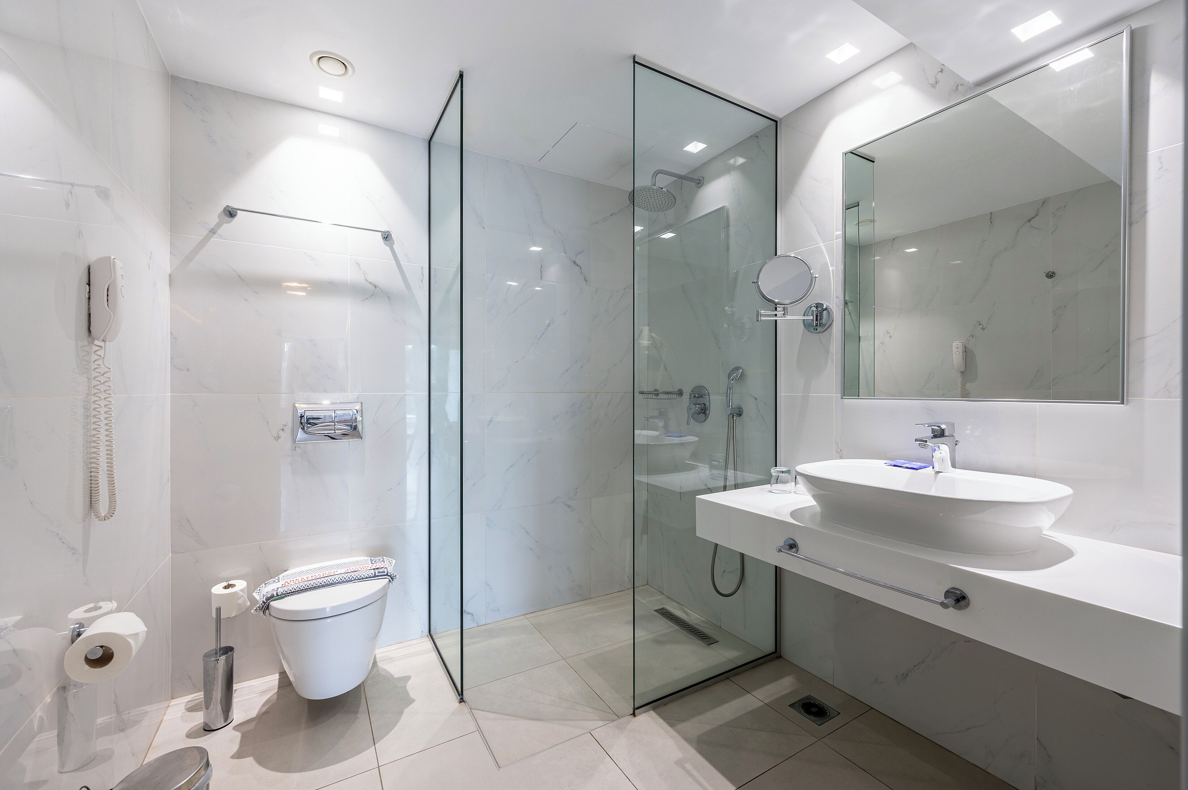 A modern bathroom with a glass-enclosed shower, a white sink, and a large mirror.