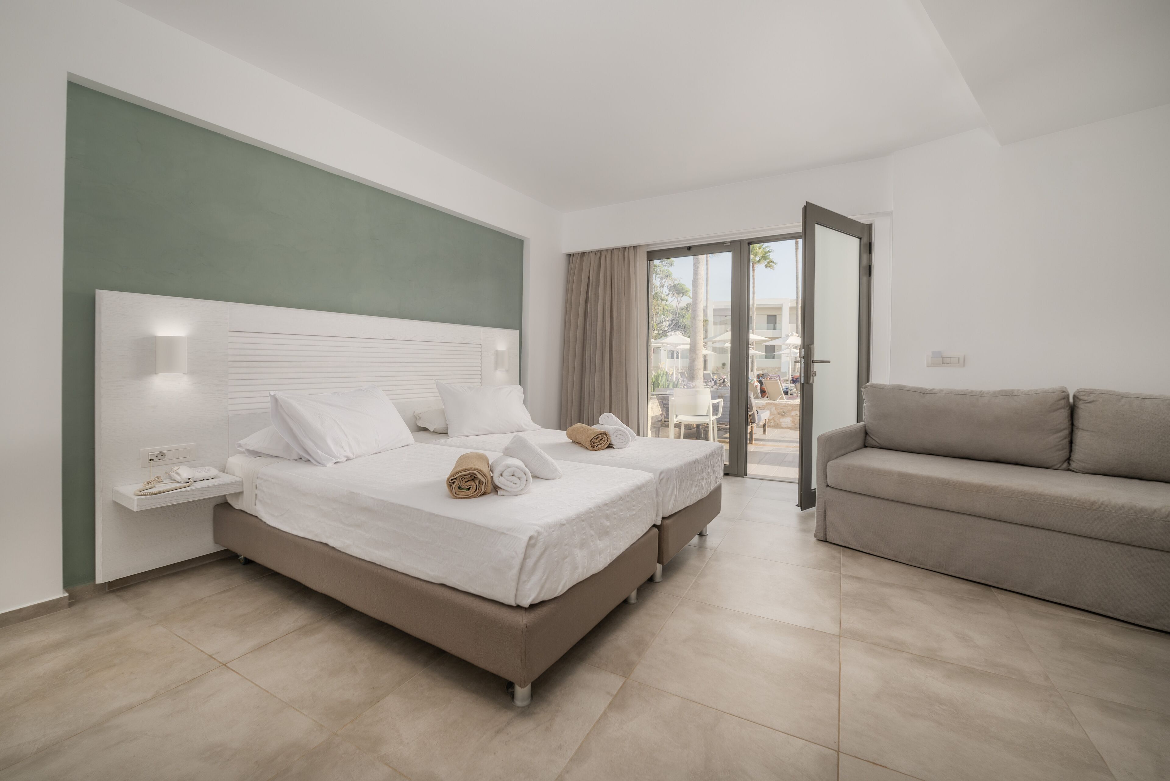 A modern hotel room with a large bed, a sofa, and a balcony with a view.