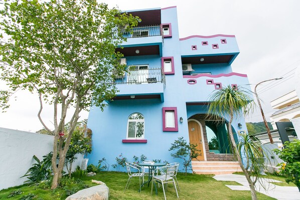 A multi-story building with a blue facade, balconies, and a small garden area with a table and chairs. - Ola B&B - Peng's family (Taitung)