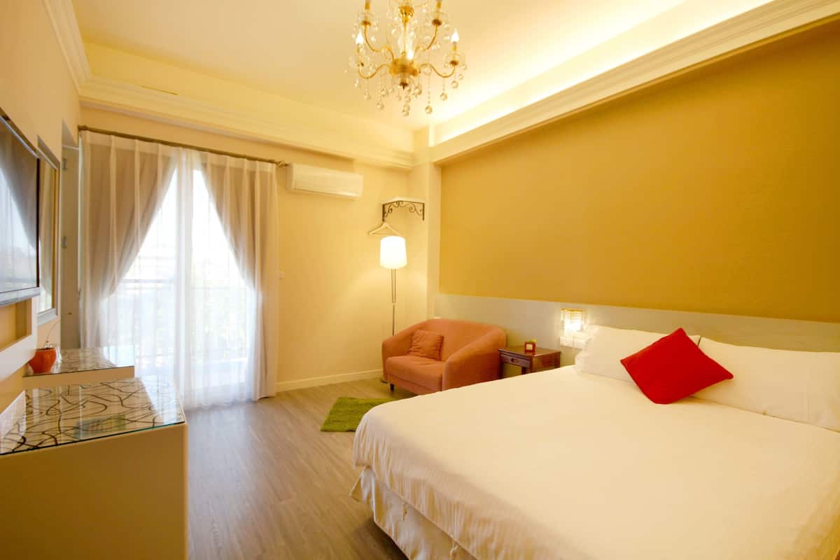 A hotel room with a bed, a chair, a desk, and a chandelier.