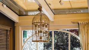 A room with patterned armchairs, a wooden ottoman, and a large window with a view of trees and a brick wall. - Hotel Sommerhof (Gosau)