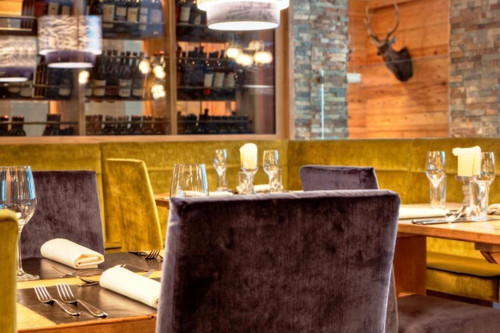 Ein Restaurantinneres mit Samtsesseln, einem Holztisch und einem Weinkühlschrank im Hintergrund.