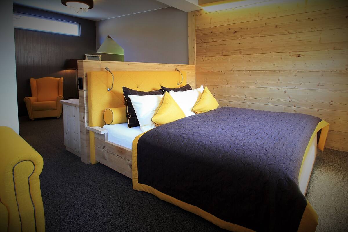 A bedroom with a bed, a chair, a bedside table, and a wooden wall.