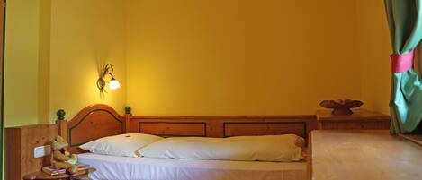 A single bed with a wooden headboard, a bedside table with a lamp, and a teddy bear on the nightstand.