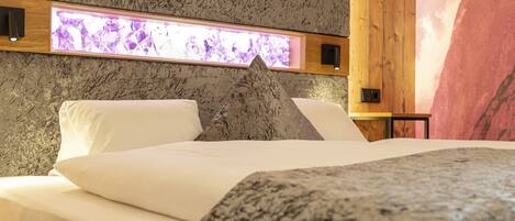 A bed with white linens and a gray headboard in a room with a textured wall and a wooden panel.