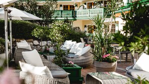An outdoor seating area with wicker furniture, cushions, and potted plants. - Hotel Sommerhof (Gosau)