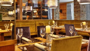 A restaurant interior with wooden tables, cushioned chairs, and hanging pendant lights. - Hotel Sommerhof (Gosau)