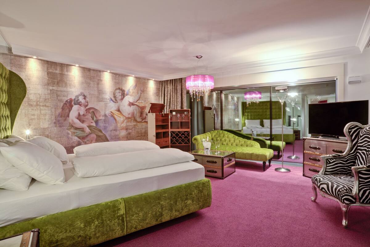 A modern living room with a green sofa, a zebra-patterned chair, a flat-screen TV, and a mural on the wall.