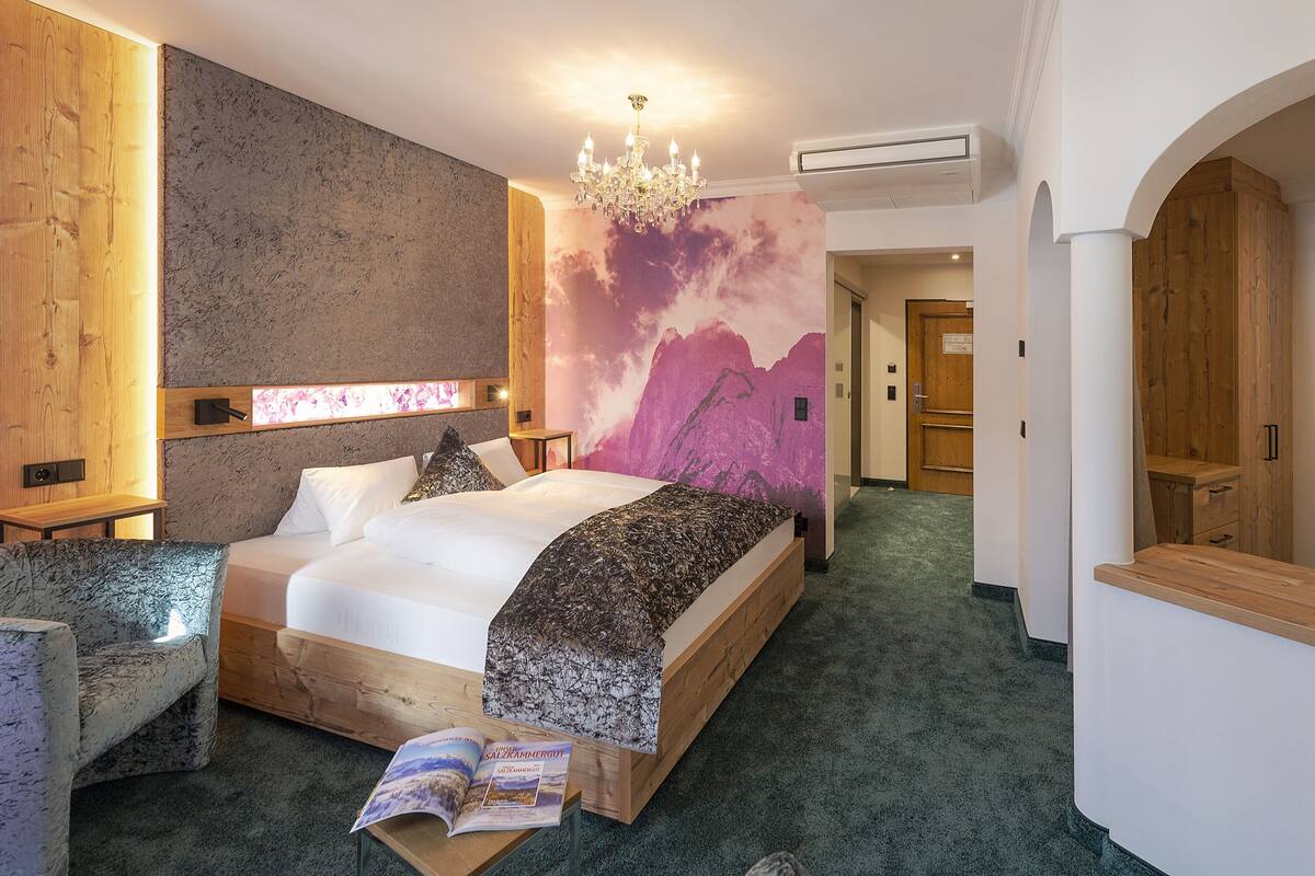 A hotel room with a large bed, a wooden headboard, a chandelier, and a wall mural.