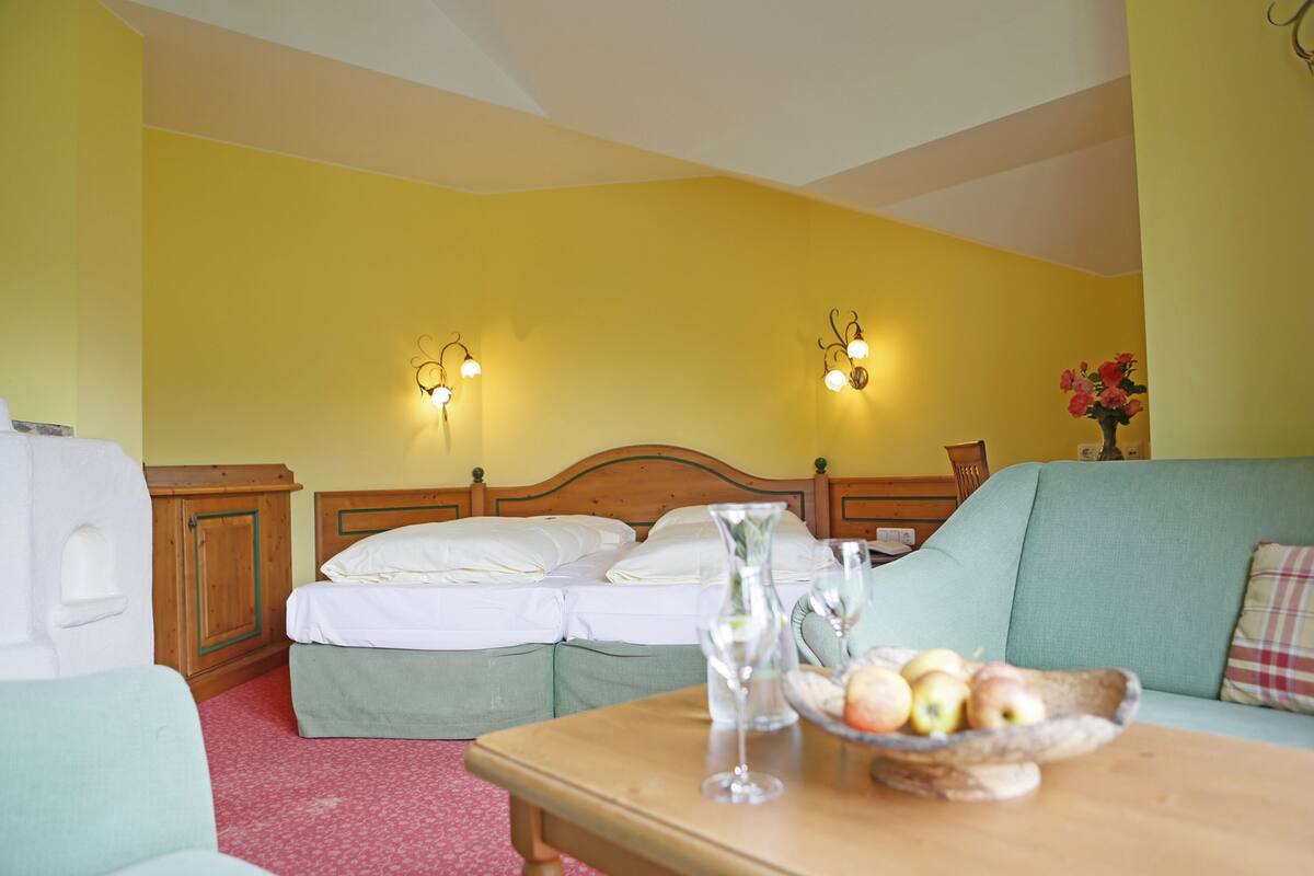 A hotel room with two beds, a wooden headboard, a table with a bowl of fruit, and two wall-mounted lamps.