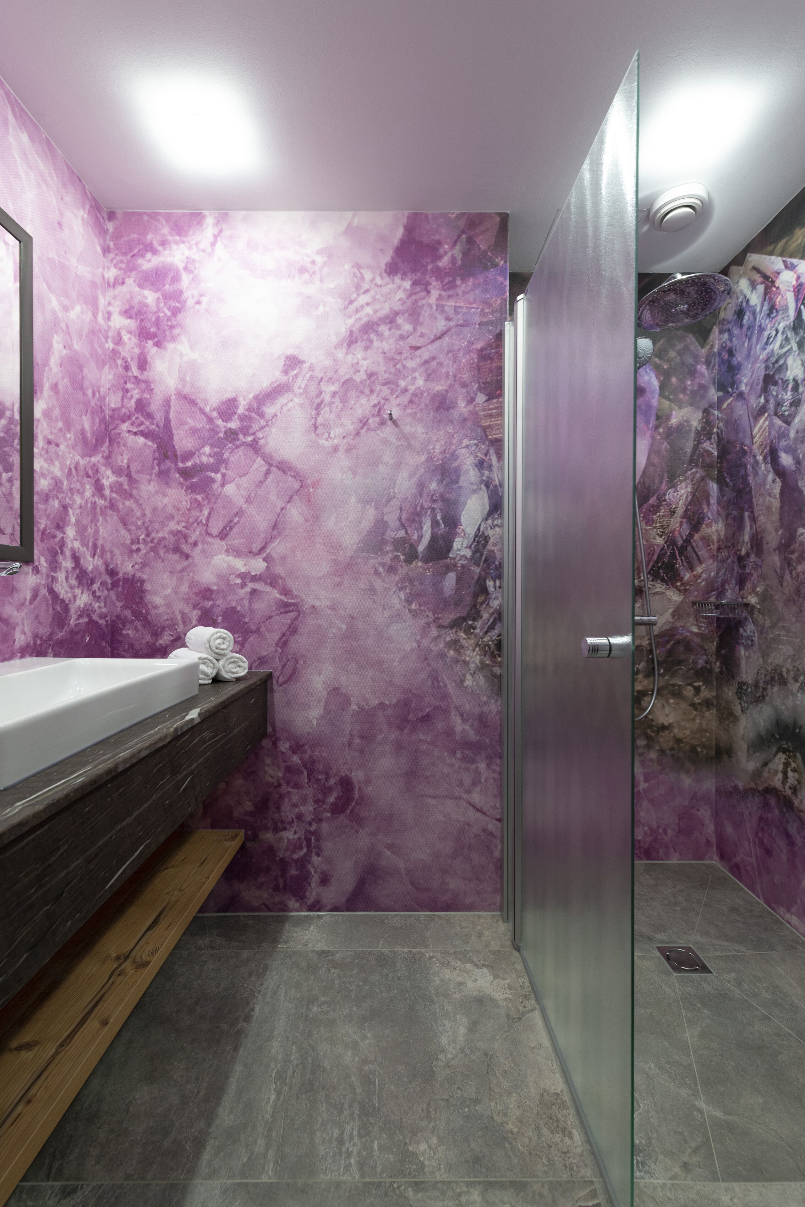 Baño con pared de mármol, cabina de ducha de vidrio y tocador de madera.