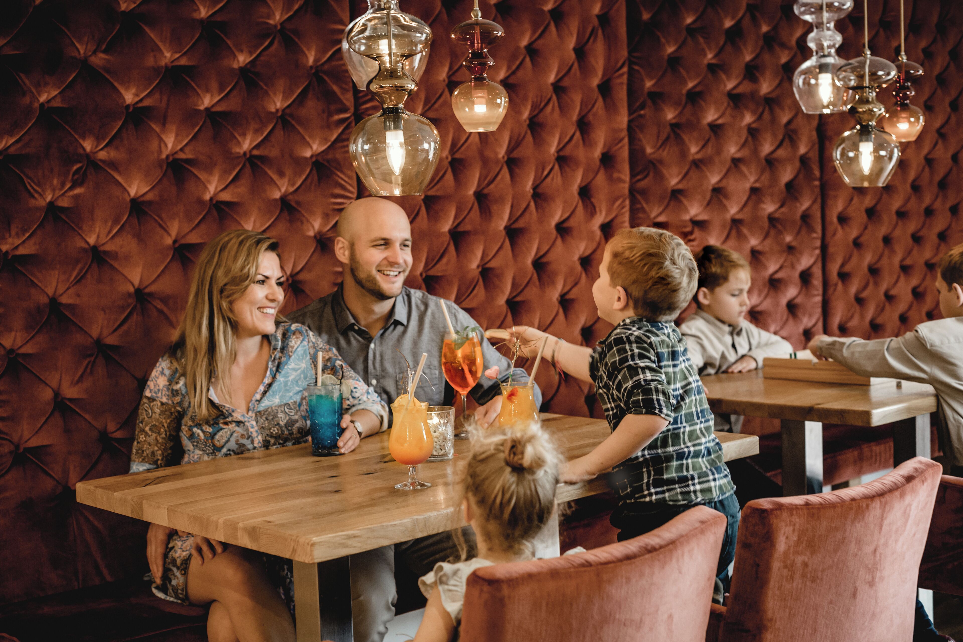 Uma família jantando em um restaurante com parede marrom texturizada e mesas de madeira.