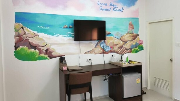 Una habitación con un mural que representa una escena de playa, un escritorio con una silla, un televisor y un refrigerador pequeño.