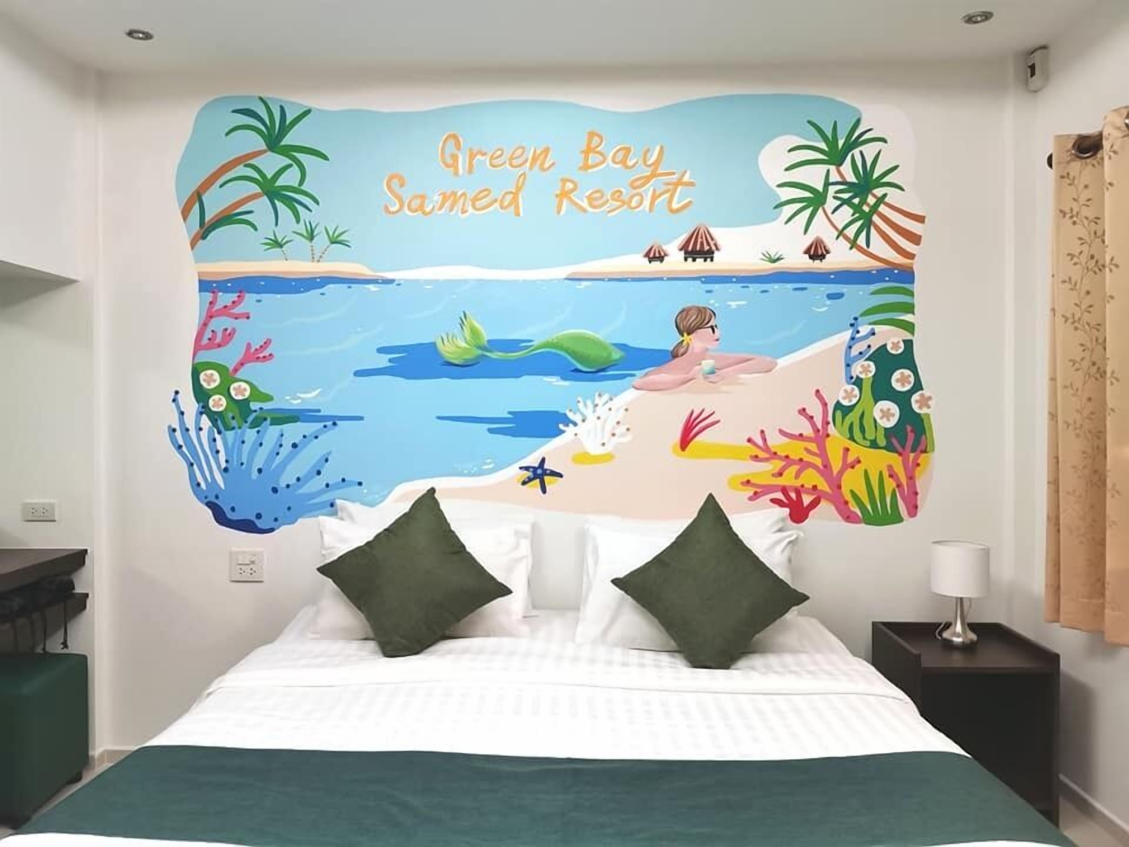 A bedroom with a mural of a beach scene, a bed with white bedding and green pillows, and a nightstand with a lamp.
