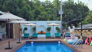 A pool area with a rectangular pool, green lounge chairs, umbrellas, and a large inflatable rabbit statue. - Green Bay Samed Resort (Rayong)