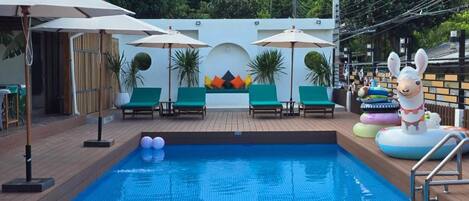A swimming pool with lounge chairs and umbrellas, surrounded by greenery.