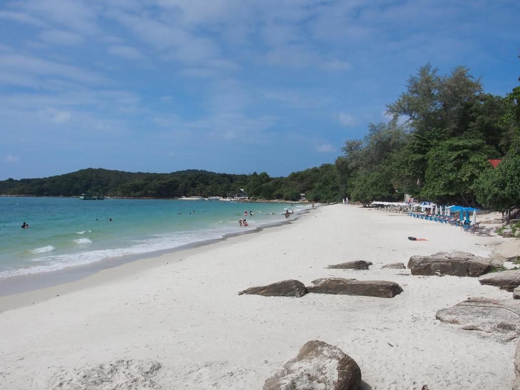 A beach with clear water, rocks, and a distant hill.