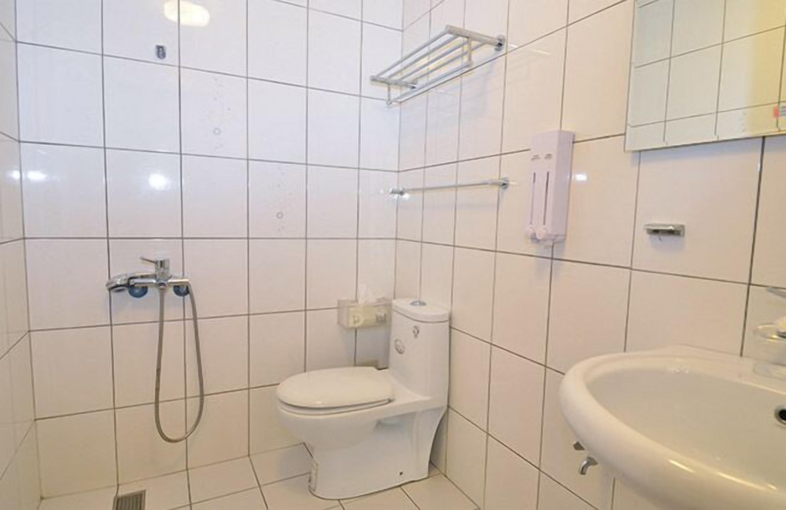 A bathroom with white tiles, a toilet, a sink, and a shower.
