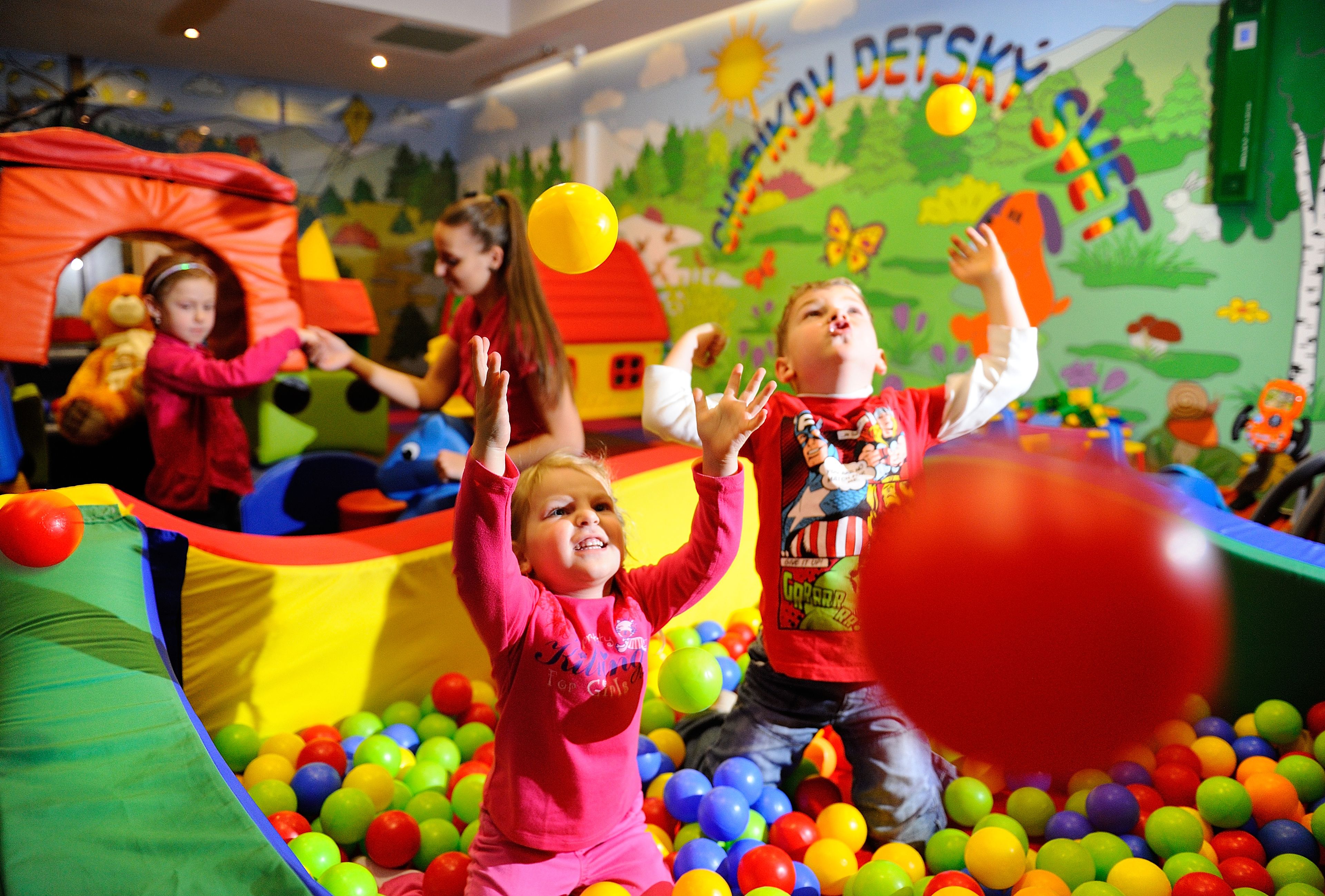 Children playing in a colorful indoor play area with a ball pit and inflatable structures.