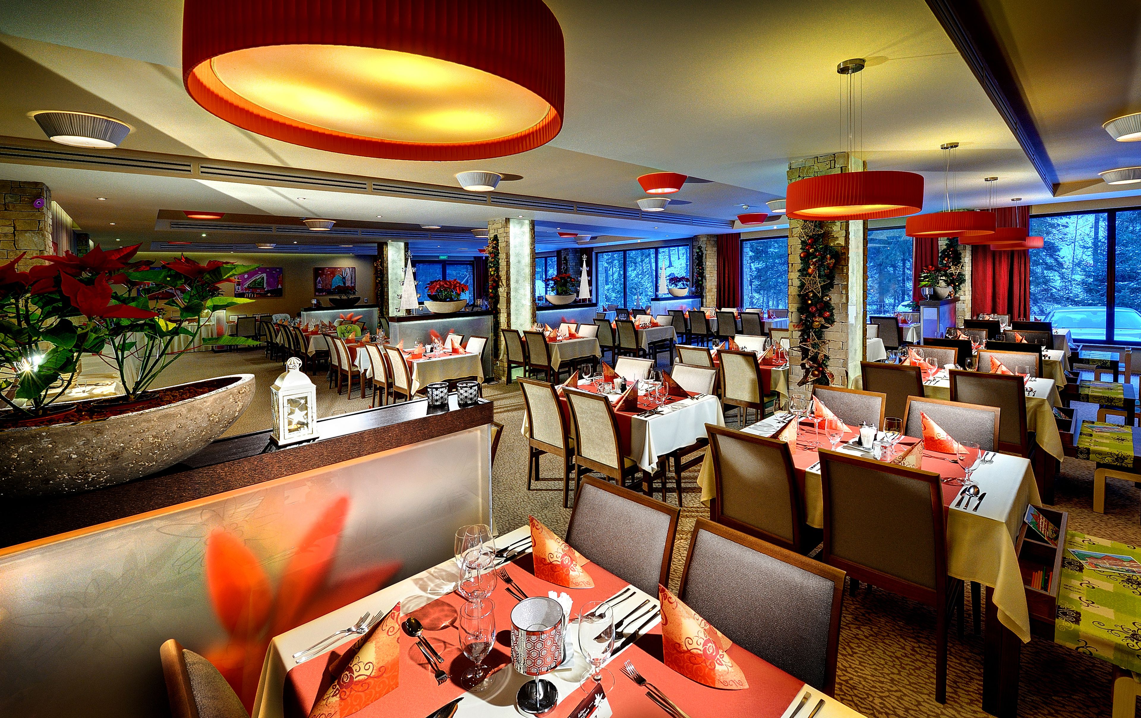 A restaurant with multiple dining tables, chairs, and red pendant lights.