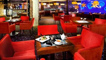 En restaurang med röda stolar och bord, en bardisk och dekorativa taklampor.