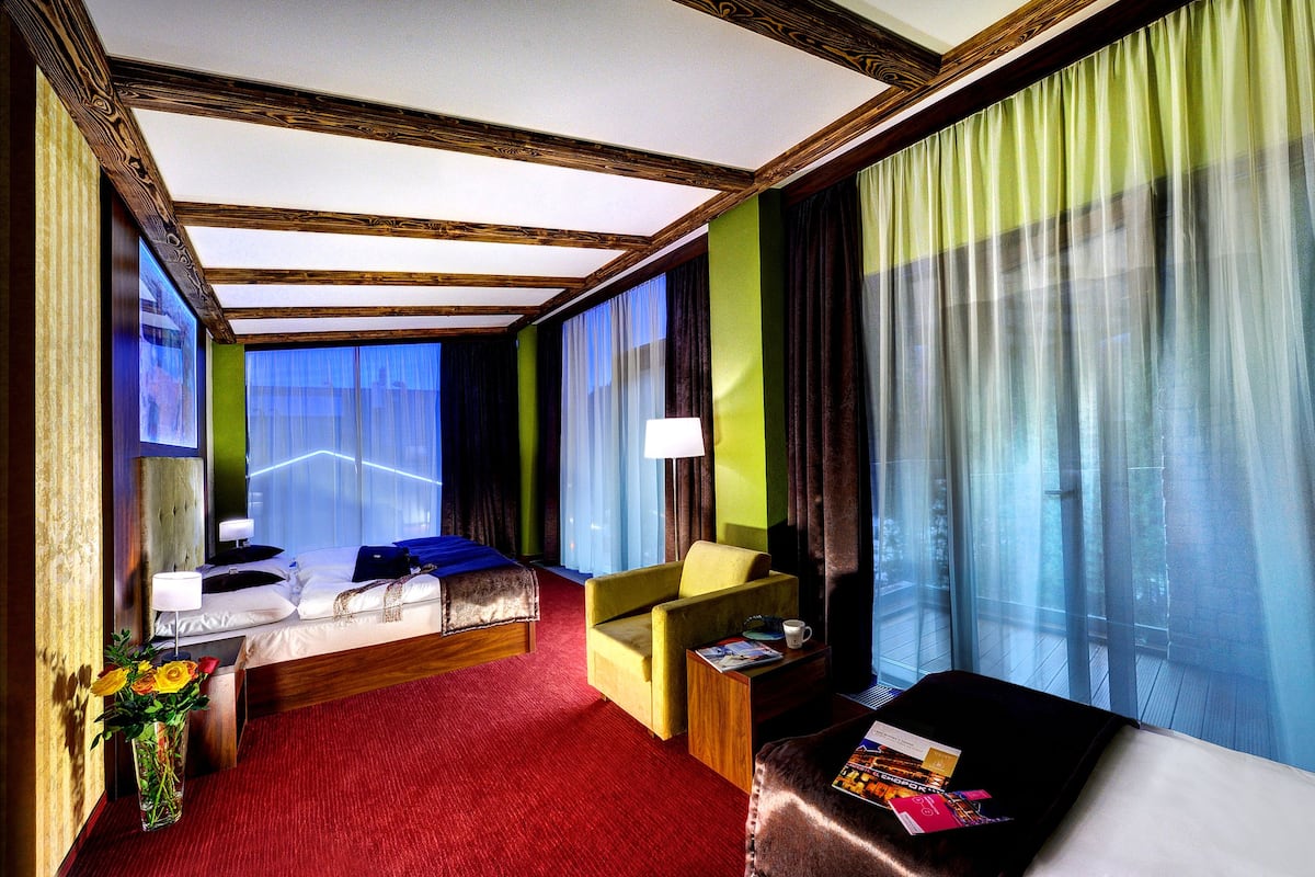 Une chambre d’hôtel avec un lit, un canapé, une petite table avec une lampe et une fenêtre avec des rideaux.