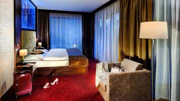 A hotel room with a bed, a sofa, a desk, a lamp, a suitcase, and a pair of shoes.