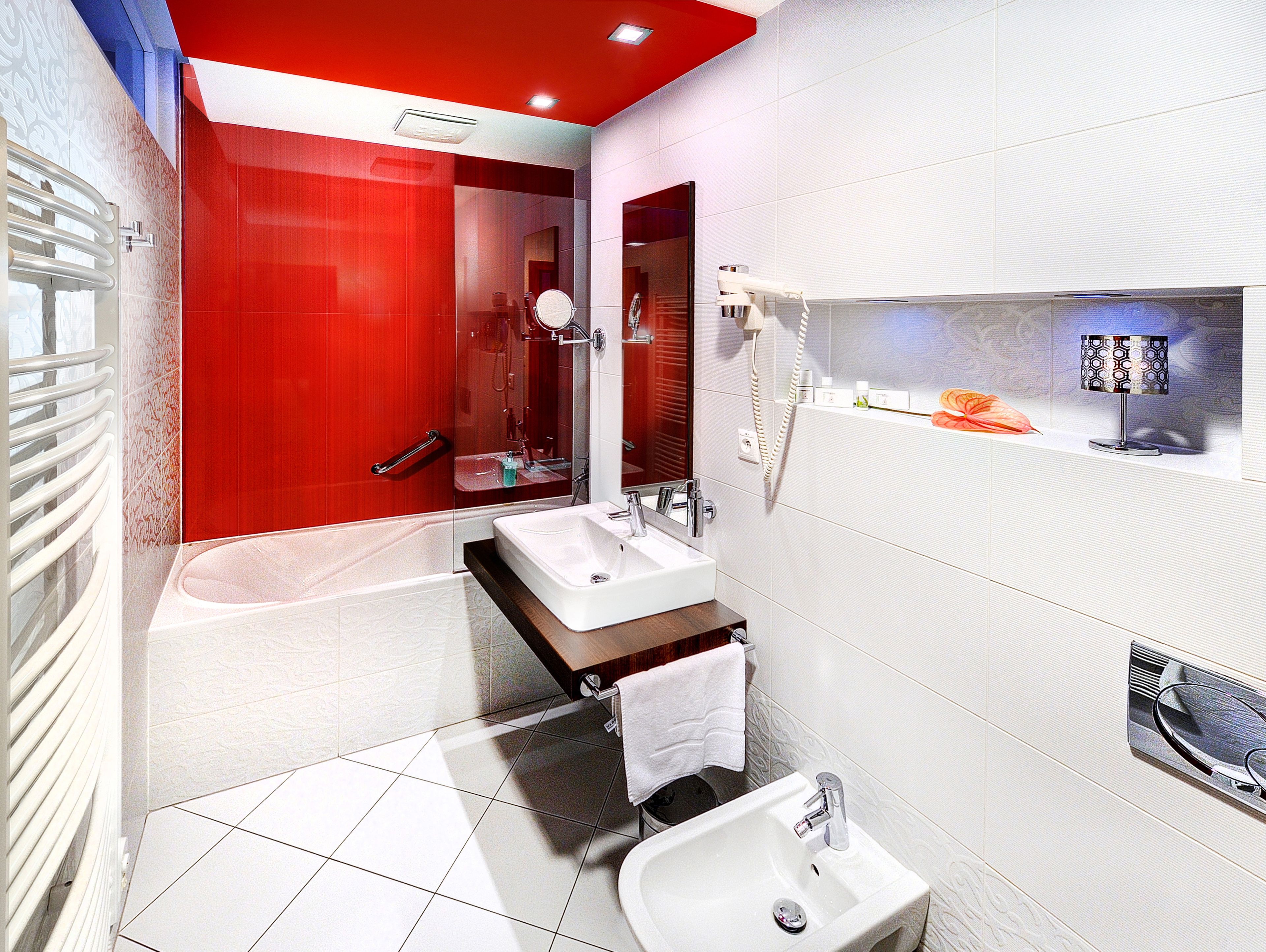 A modern bathroom with a red accent wall, a bathtub, a sink, and a mirror.