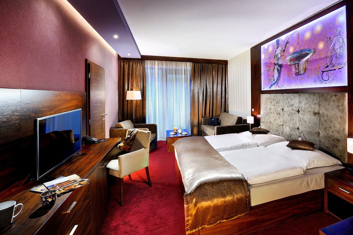 Une chambre d’hôtel avec un grand lit, un bureau avec un ordinateur, une télévision et un mur en pierre.