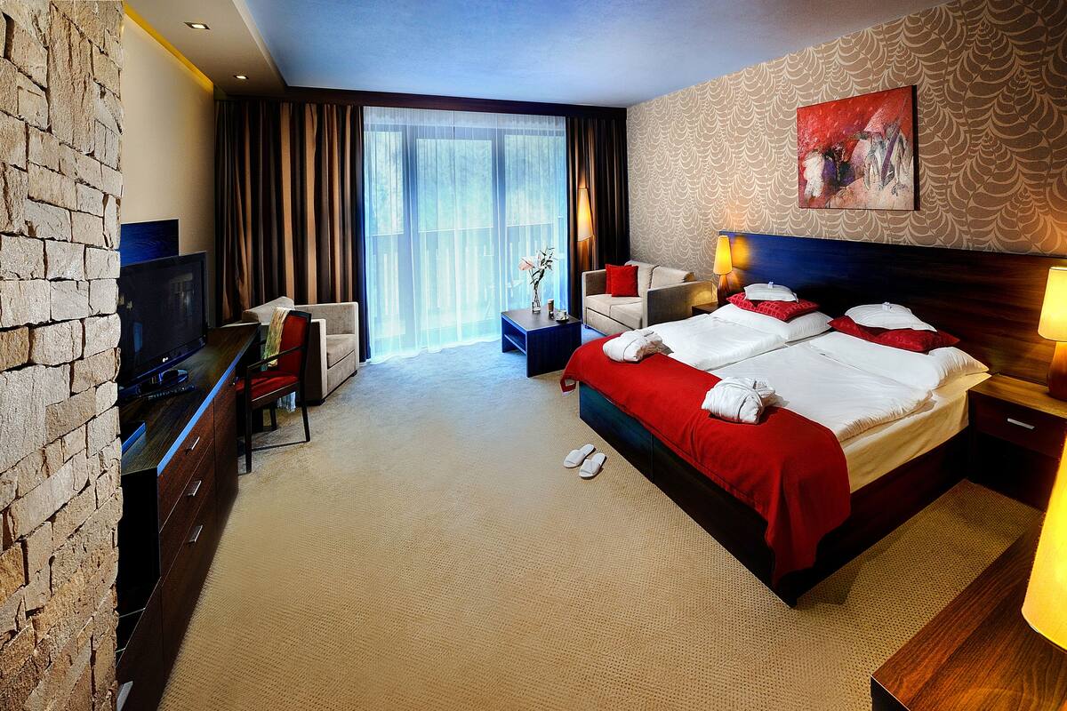 Une chambre d’hôtel avec un mur en briques, une télévision, un bureau, un lit avec une literie rouge, une table de chevet avec une lampe et un tableau accroché au mur.