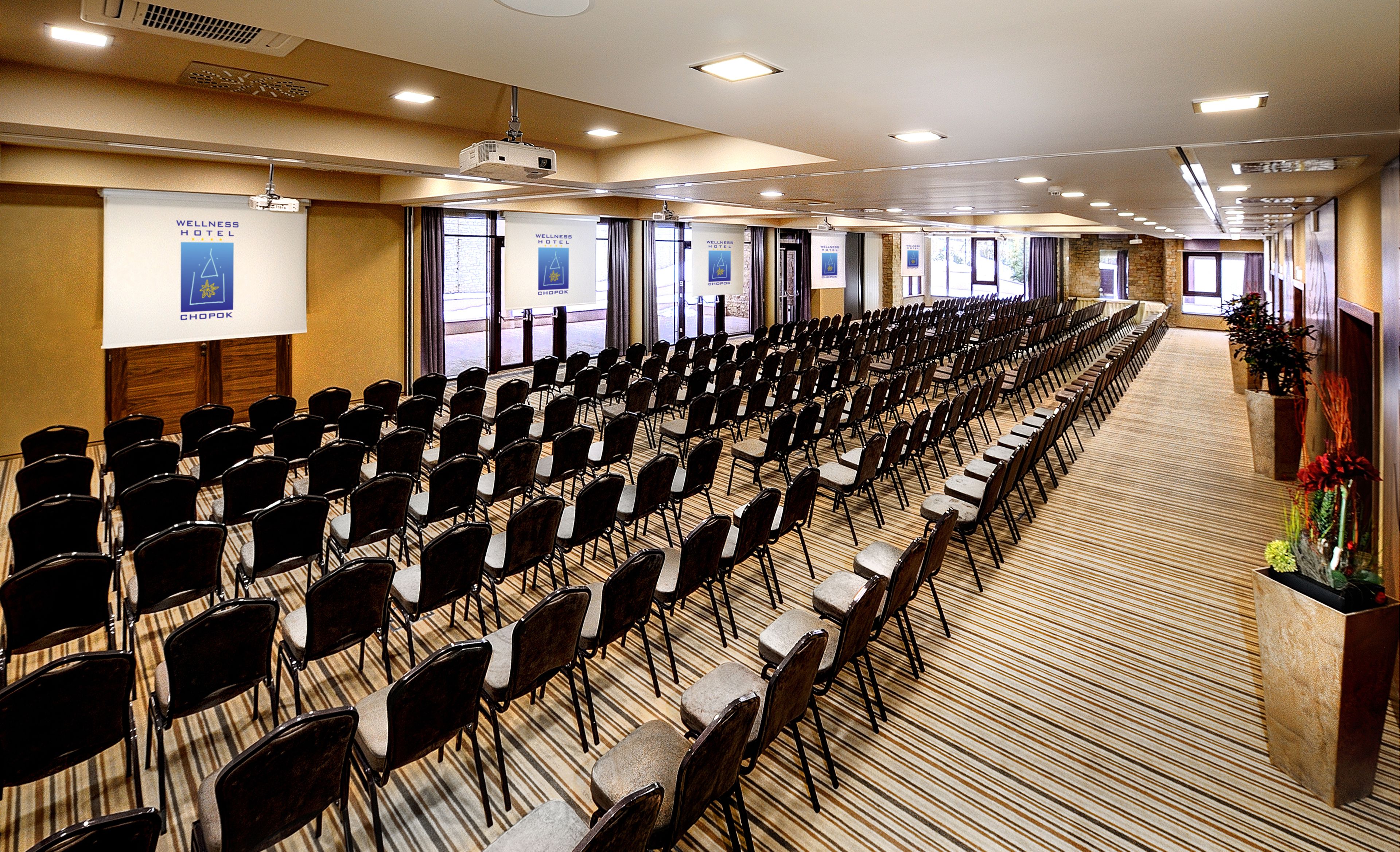 A conference room with rows of chairs, a projector, and banners for Wellness Hotel Chopok.