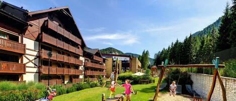 A hotel with multiple balconies, a playground, and a view of the surrounding forest.