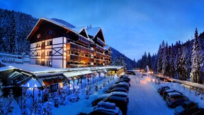 Hotel coberto de neve com várias varandas e área de estacionamento.