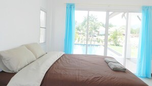 Un dormitorio con una cama grande, una ventana y vistas a una piscina y vegetación.